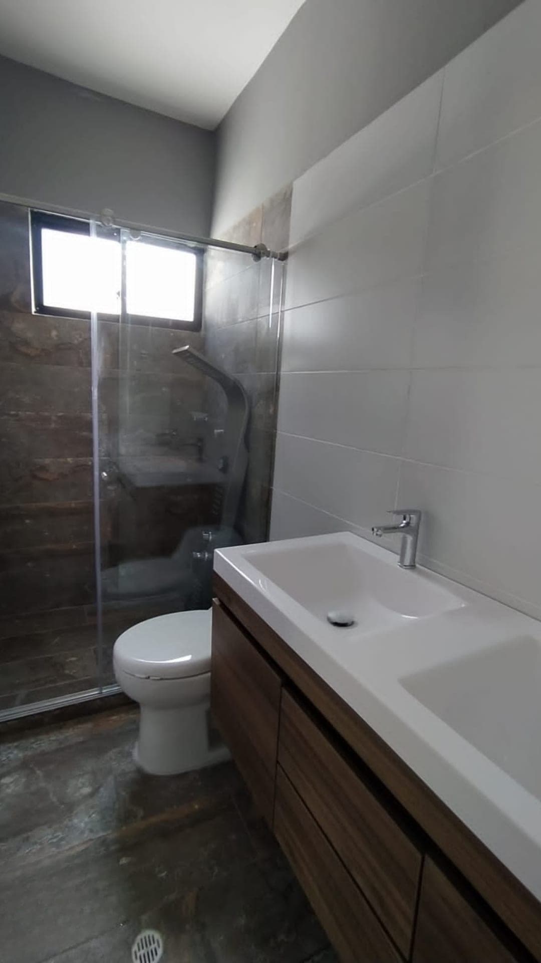 Baño terminado con ducha en vidrio, enchape en cerámica y mueble flotante en madera