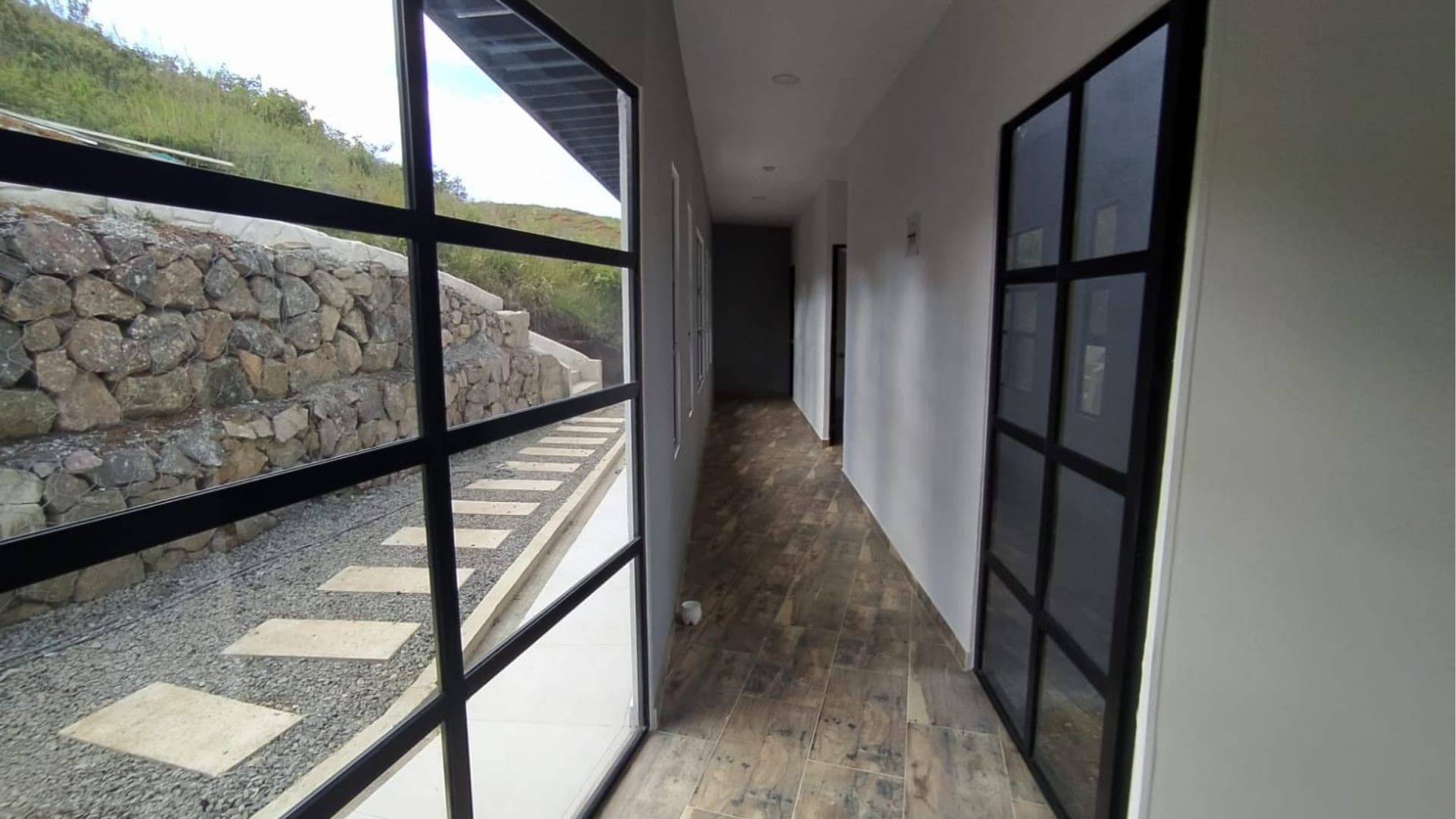 Pasillo interior con ventanal de piso a techo frente a un muro en piedra