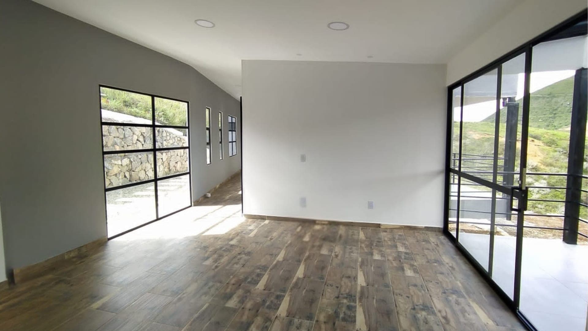 Sala de una vivienda Fabrique con ventanales de piso a techo en aluminio negro y piso en gres símil madera